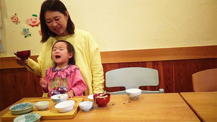 食事の途中母親の膝の上で満足そうな笑顔をみせる幼児