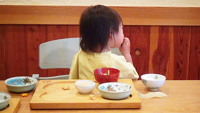 2歳の幼児が手づかみで後ろを向いて食事をしている様子